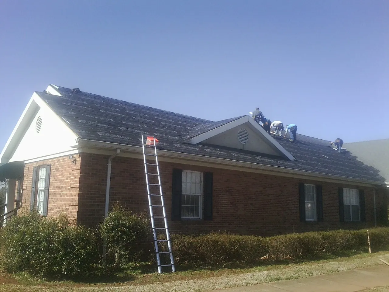 Crew tearing shingles off a brick ranch roof with a ladder set — Metal Roof Repair work by our crew in Lagrange