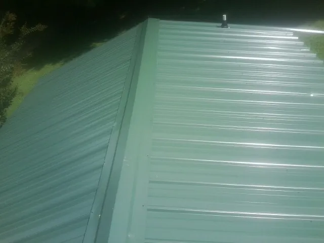 New green metal panels meeting at the ridge of a roof — Flat Roof Repair work by our crew in Lagrange