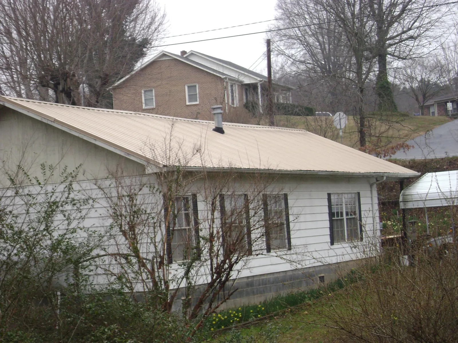 Tan metal roof on a white sided house set into a hillside — Commercial Roofing by Roofing Brothers in Lagrange